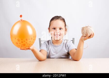 Fille souriante tenant un ballon orange et corde de jute, citrouilles à faire soi-même pour Halloween, passe-temps auto-isolation Banque D'Images