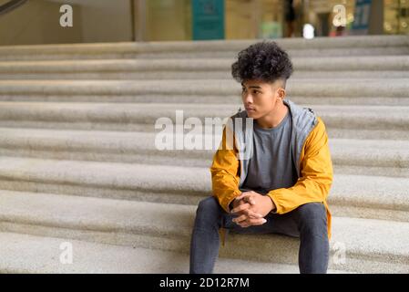 Jeune homme asiatique aux cheveux bouclés assis sur l'escalier la ville Banque D'Images