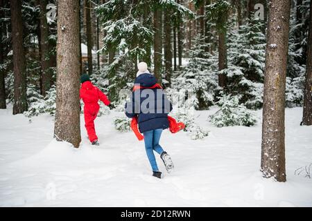 Fille et garçon en vêtements d'hiver courant dans la neige forêt d'hiver, vue arrière. Banque D'Images