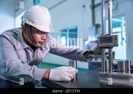 Travailleur de technicien asiatique portant une combinaison de sécurité et un contrôle de qualité avec un produit de masse à jauge de hauteur sur une plaque de surface en granit dans une usine industrielle. Banque D'Images