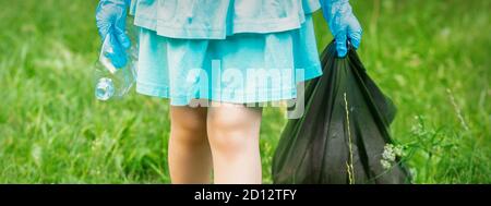 Petite fille avec une bouteille en plastique froissé et un sac poubelle ses mains tout en nettoyant les ordures dans le parc Banque D'Images