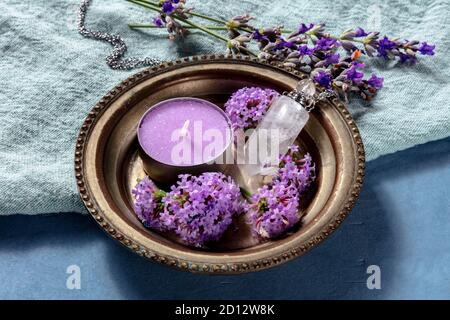 Rituel païen. Une bougie pourpre, un charme cristal, et des fleurs, vervain et lavande sur un fond bleu Banque D'Images