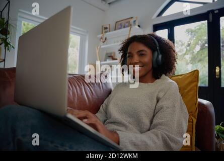Joyeuse jeune femme africaine se détendant à la maison regardant la série web avec un casque assis sur un canapé Banque D'Images