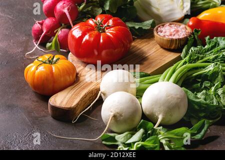 Variété de matières organiques humides frais tomates légumes colorés, avec des feuilles de radis, fenouil, paprika, sel pour la salade sur planche en bois foncé dessus Banque D'Images