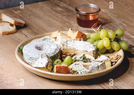 Plateau de fromages assortiment de fromages français servi avec du miel, noix, pain et raisins sur plaque en céramique sur table en bois. Close up Banque D'Images