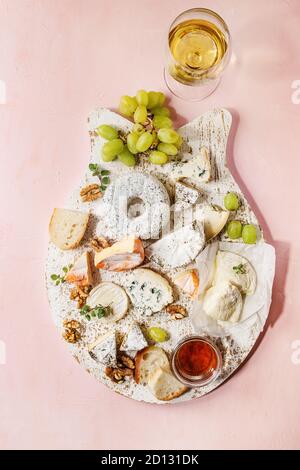 Plateau de fromages assortiment de fromages français servi avec du miel, noix, pain et raisins sur servant en bois blanc avec du verre de vin blanc sur Rose Banque D'Images