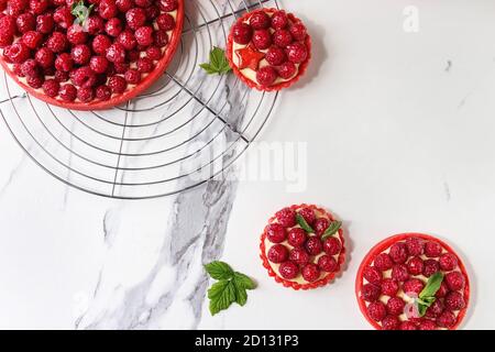 Variété de framboise rouge tartes et tartelettes sablés crème au citron et framboises fraîches servi glacé sur grille de refroidissement sur le marbre blanc textur Banque D'Images