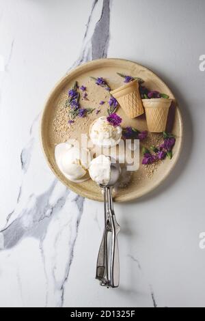 Boules de crème glacée à la vanille fait maison servi avec des fleurs comestibles et cuillère en métal dans une plaque en céramique sur fond de marbre blanc. Vue de dessus, de l'espace. Banque D'Images