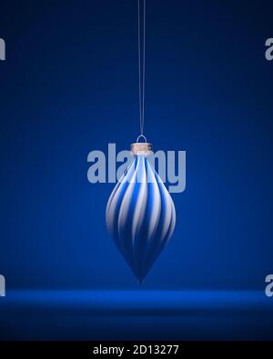 Boule de Noël blanche et bleue à motif oblong torsadé, suspendue à une corde. Fond bleu royal ombré. Décoration de Noël, concept d'atmosphère festive. Banque D'Images