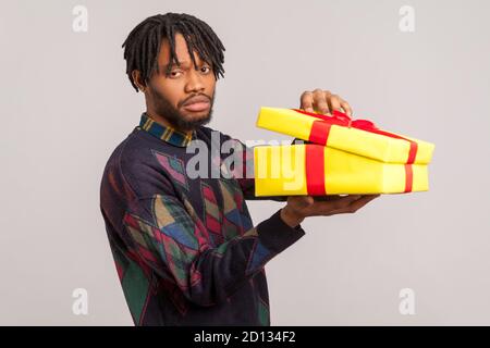 Mécontent homme africain déçu avec des dreadlocks tenant une boîte cadeau non emballé avec un visage frustré insatisfait, contrarié par le présent. Prise de vue en studio I Banque D'Images