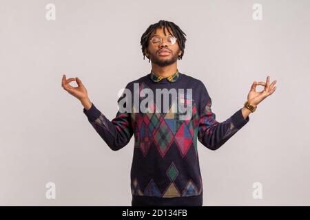 Paisible homme africain calme avec des dreadlocks dans des verres debout avec les yeux fermés et le geste mudra, méditant essayant de se concentrer, inspiration. Indoo Banque D'Images