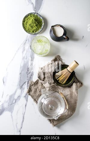 Ingrédients pour la glace matcha faisant boire. Le thé vert matcha en poudre dans un bol en céramique, traditionnel bambou cuillère, fouet, lait, théière en verre, sur des glaçons. Banque D'Images