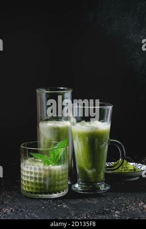 Thé vert matcha latte glacé ou cocktail dans trois différents verres à la menthe, des cubes de glace et la poudre de matcha au fond texture sombre Banque D'Images