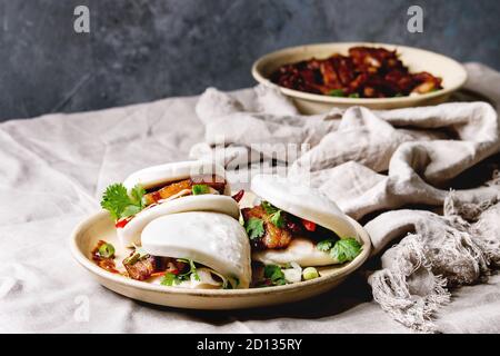 Sandwich asiatique brioches bao gua à la vapeur avec du porc, du ventre et des légumes verts servi dans une plaque en céramique sur table avec nappe en lin. Fo rapide de style asiatique Banque D'Images