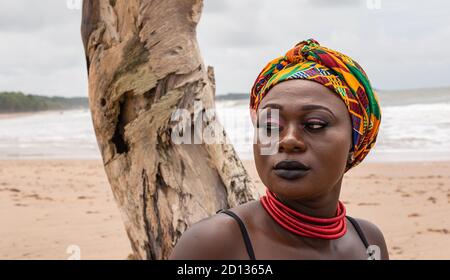 Femme africaine ghanéenne avec une coiffure colorée assise à un cassé le palmier se trouve à la plage de l'Axim Ghana West Afrique Banque D'Images