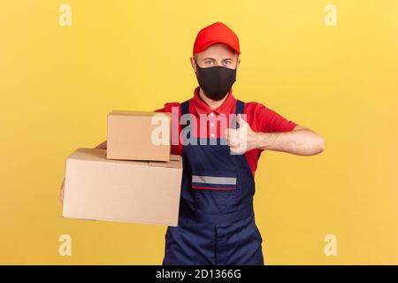 Courrier positif en uniforme et masque hygiénique tenant des colis de carton montrant les pouces vers le haut, satisfait du service rapide, livraison express sur la quarantaine Banque D'Images