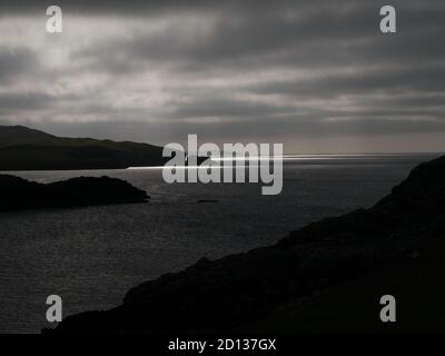 En noir et blanc, une vue sombre et menaçante de la lumière du soleil sur l'eau à travers Magnus Bay depuis le flanc de colline à Islesburgh près de Mavis Grind, Shetland, Royaume-Uni. Banque D'Images