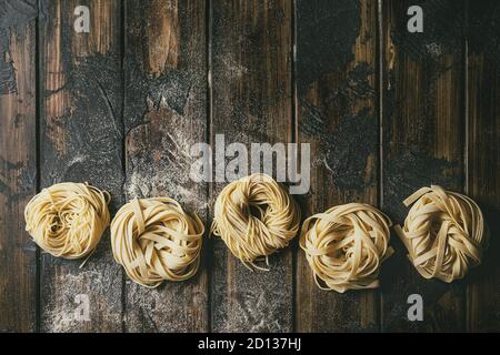Variété de matières premières maison italienne spaghetti tagliatelle Pâtes alimentaires non cuites et en ligne avec plus de farine de semoule de planches en bois sombre texture table. Mise à plat, co Banque D'Images