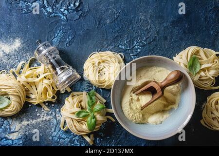 Variété de matières premières maison italienne spaghetti et tagliatelle Pâtes alimentaires non cuites avec des feuilles de basilic, huile d'olive, sel, poivre, farine de semoule sur bleu foncé tex Banque D'Images