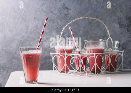 Fruits rouges baies pastèque cocktail glacé en verres avec paille rayée sur table en marbre blanc avec mur gris à l'arrière-plan. Boisson fraîche d'été. Banque D'Images