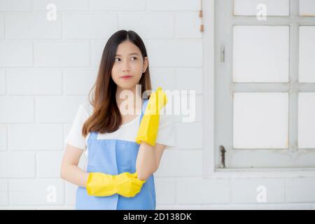 Portrait la jeune femme asiatique est gouvernante dans des gants en caoutchouc et un tablier pour la protection à la maison, uniforme de femme de ménage, nettoyage et lavage, fille debout travail Banque D'Images