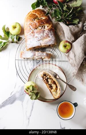 Des tranches de pâte feuilletée strudel aux pommes Tarte sur grille de refroidissement servi avec des pommes mûres, branches, le sucre en poudre, tasse de thé plus de texte en marbre blanc Banque D'Images