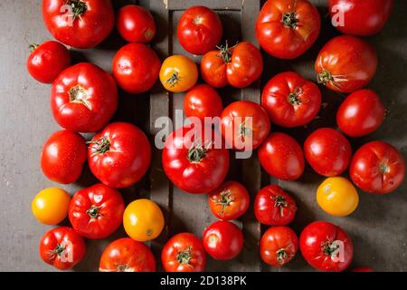 Variété de tomates fraîches mûres jardinage biologique différents types et couleurs avec de l'eau sur place old grey background. Mise à plat, de l'espace Banque D'Images