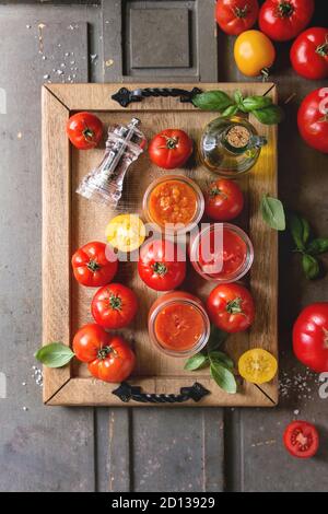 Variety of three homemade tomato sauces in glass jars with ingredients above. Different kinds of tomatoes, basil, olive oil, pepper, salt in wood tray Banque D'Images
