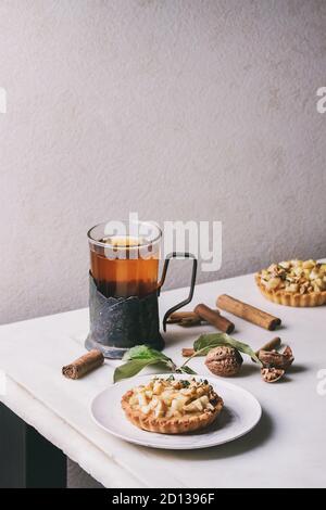 Sablés aux pommes faite maison à tartelette plaque blanche, verre de thé chaud en vintage support de tasse avec des bâtons de cannelle, noix, pommes branches ci-dessus sur Banque D'Images