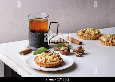 Sablés aux pommes faite maison à tartelette plaque blanche, verre de thé chaud en vintage support de tasse avec des bâtons de cannelle, noix, pommes branches ci-dessus sur Banque D'Images