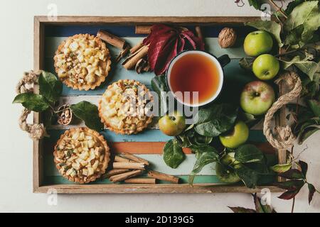 Tartelettes sablés aux pommes faite maison avec des bâtons de cannelle, noix, pommes de branches, tasse de thé dans le bac en bois coloré sur fond de marbre blanc Banque D'Images