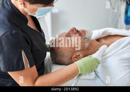 Esthéticienne professionnelle faisant la procédure de rajeunissement de la peau pour son client Banque D'Images