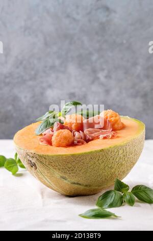 Melon et jambon cru ou salade de prosciutto servi dans la moitié de melon cantaloup, décoré par le basilic frais debout sur nappe blanche. Banque D'Images