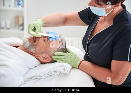 Travailleur de spa professionnel effectuant une procédure de soin de la peau pour un homme vieillissant Banque D'Images