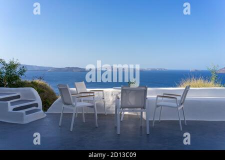 Quatre chaises blanches avec table blanche sur la terrasse blanche avec vue sur la mer bleue et la caldeira par jour ensoleillé, sans personne. Oia, île de Santorin, Grèce Banque D'Images