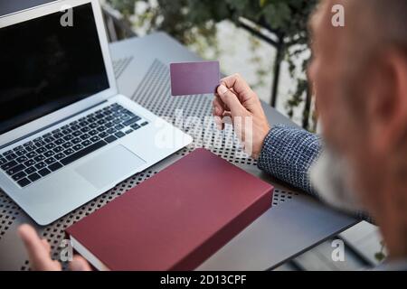 Homme d'affaires avec une carte en plastique dans la main assis avec un ordinateur portable Banque D'Images