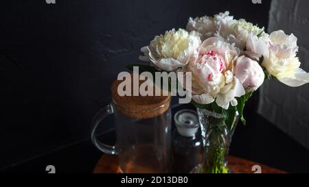 Des pivoines blanches magnifiques et luxuriantes dans un vase sur fond noir, bouquet à la maison. Banque D'Images