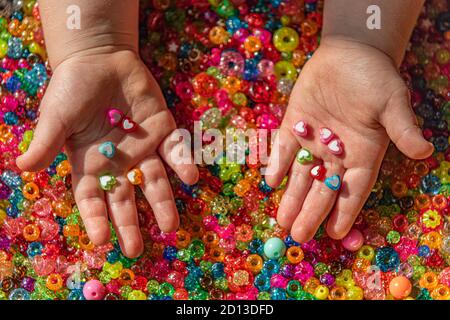 Perles de couleur dans les paumes de l'enfant. Un fond très coloré de perles étincelantes Banque D'Images