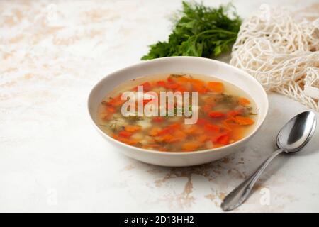 Soupe de poisson chaud avec pommes de terre, poivrons rouges, carottes et légumes verts dans une assiette légère sur fond clair. Espace pour le texte Banque D'Images