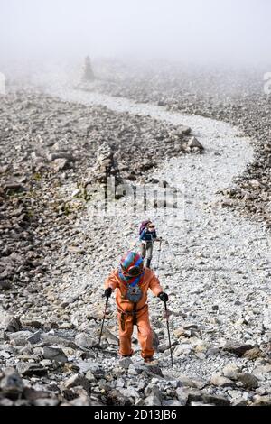 Lloyd Scott, collecteur de fonds vétéran, qui tente de grimper les trois sommets tout en portant un costume de plongée en haute mer, est suivi par un membre de son équipe de soutien lors de son défi sur Ben Nevis en Écosse. Banque D'Images
