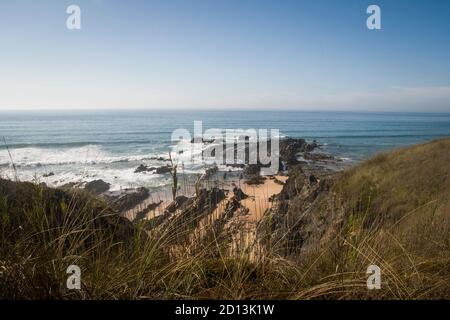 Paysage de plage avec des vagues venant à terre et des falaises entrant dans le sable, sous un ciel bleu et une journée ensoleillée. Vue depuis le dessus des falaises Banque D'Images