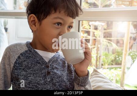Un garçon asiatique a soif d'eau potable d'une tasse en plastique blanc. Banque D'Images