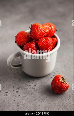 Fraises mûres rouges dans une tasse grise sur fond gris gros plan. Photo de nourriture Banque D'Images