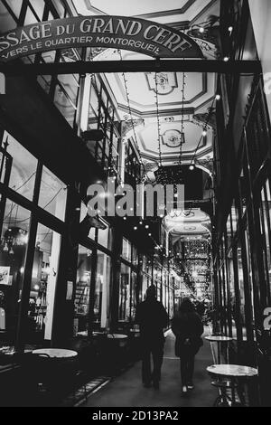 PARIS, FRANCE - 7 DÉCEMBRE 2019 : les gens magasinent dans une arcade couverte historique du Grand-Cerf décorée pour les vacances de Noël. Photo noir et blanc Banque D'Images