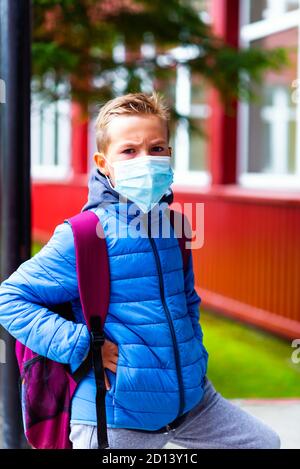 Un écolier en colère portant un masque de protection décontracté et portant un sac à dos près de l'école. Enfants qui vont à l'école après une pandémie, les élèves le sont Banque D'Images