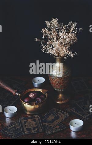 Sombre, moody, ésotérique, photo occulte de décoration en laiton, vase avec fleurs blanches, cartes de tarot dessinées à la main sur table en bois. Noir et or Banque D'Images