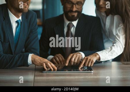 Des collègues heureux utilisant la même tablette numérique ensemble. Deux hommes et une femme travaillent au bureau. Image rognée. Se concentrer de manière sélective sur les mains des professionnels Banque D'Images