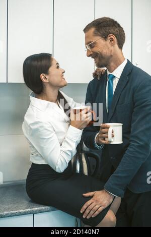 Couple buvant du café et flirtant pendant le déjeuner. Homme et femme souriants tiennent des tasses de boissons chaudes en regardant l'un l'autre. Concept de romance de bureau. Élevée Banque D'Images
