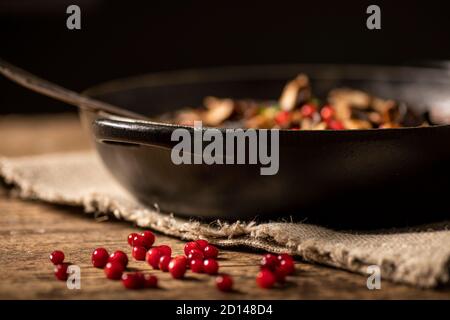 Bouquet de baies de lingonis placées sur une table rustique en bois. Pot noir avec nourriture en arrière-plan. Faible profondeur de champ. Banque D'Images