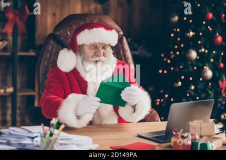 Photo cheveux gris étonnés santa claus s'assoient table dans la fée north-pole maison lire x-mas noël liste de souhaits enfant impressionné cadeau présenter le cache d'usure ask Banque D'Images